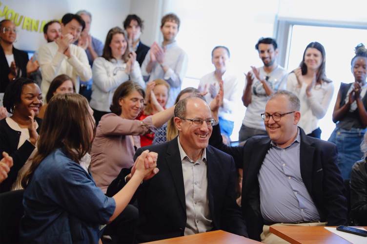 A large group of people in an office conference room clapping and smiling.