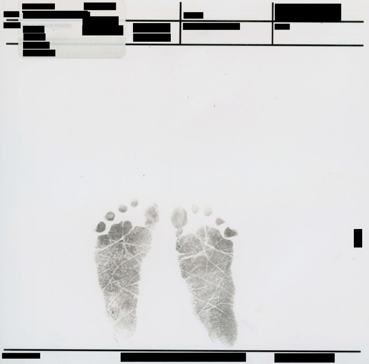 A pair of black ink footprints from an infant centered on a white page. Above and below the footprints are several rows of official form fields and identifying information, all of which have been redacted with solid black bars.