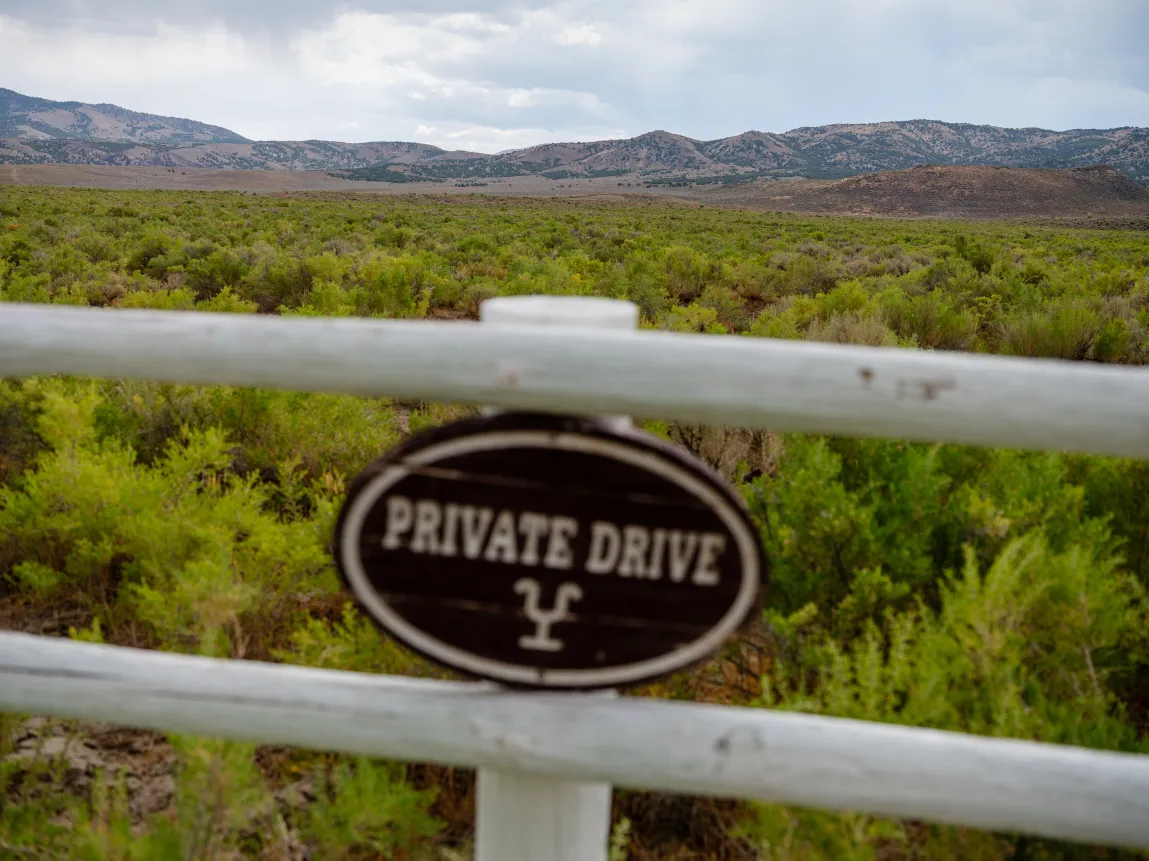 A sign on a fence noting “private drive” at the Winecup Gamble Ranch, with mountains in the background.