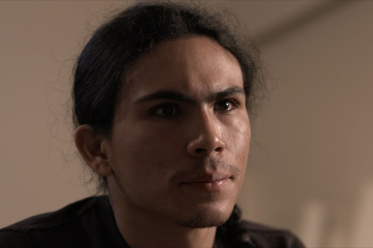 A man with his hair tied back looks past the camera.