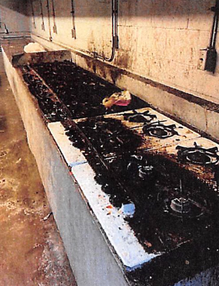 A row of stovetops covered in black grime stand in front of a dirty cinderblock wall.
