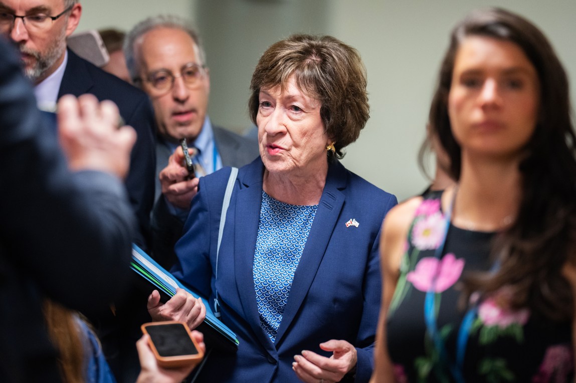 A woman wearing a navy blue pantsuit walks among reporters.