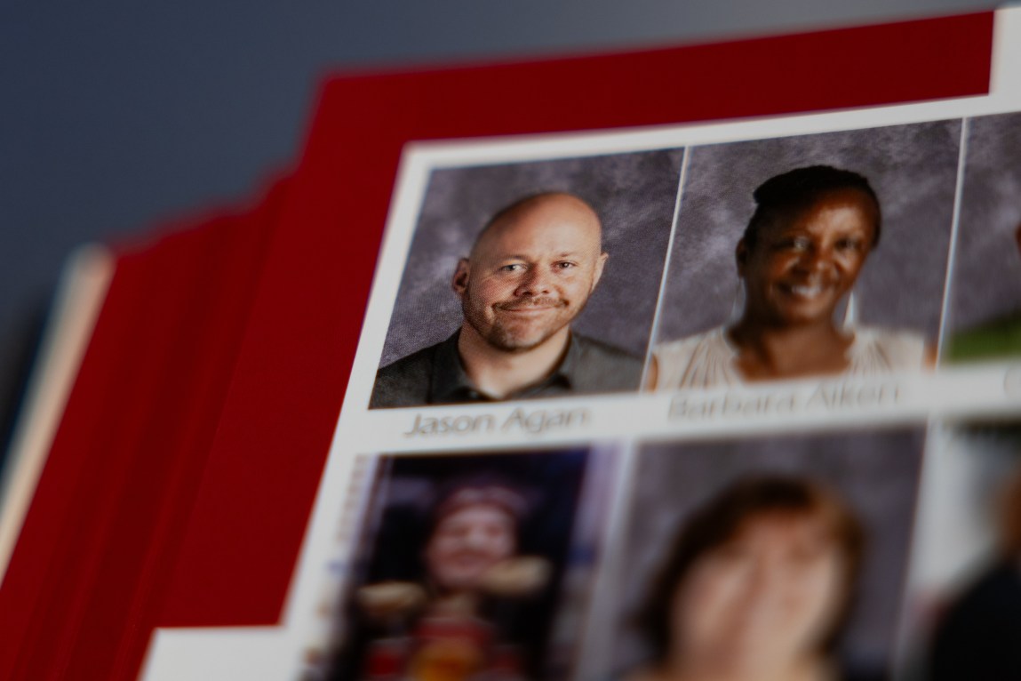 A yearbook opened to a page with a grid of headshots. One headshot is in focus and shows a man smiling at the camera. The rest of the headshots are blurry.