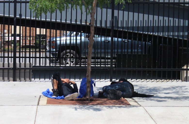 Men sleep on the sidewalk under the shade of a tree in Wilmington, Delaware, in May 2024.