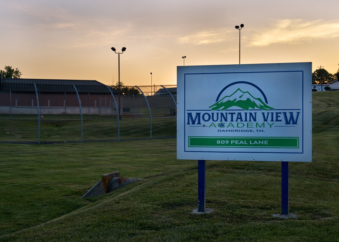 A sign reads “Mountain View Academy, Dandridge, TN” and has a logo with a mountain. Behind it is a green field and a fenced-in building.