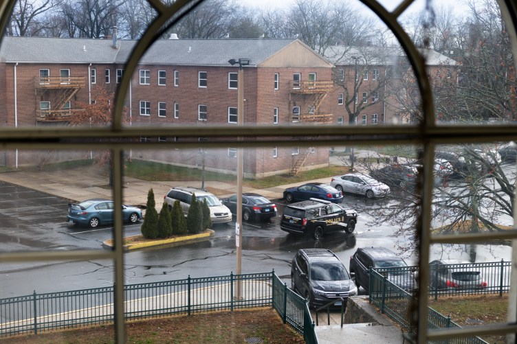 Brick buildings and trees stand next to a lot with parked cars and a black police car. The scene is framed by window panes.