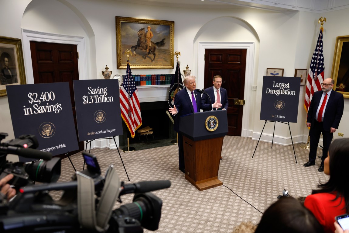 President Donald Trump gestures while speaking from a lectern in the Roosevelt Room of the White House as members of the press look on.