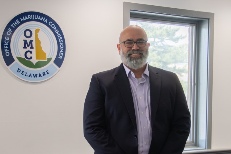 New Delaware Marijuana Commissioner Josh Sanderlin stands in front of a sign for the Office of the Marijuana Commissioner.
