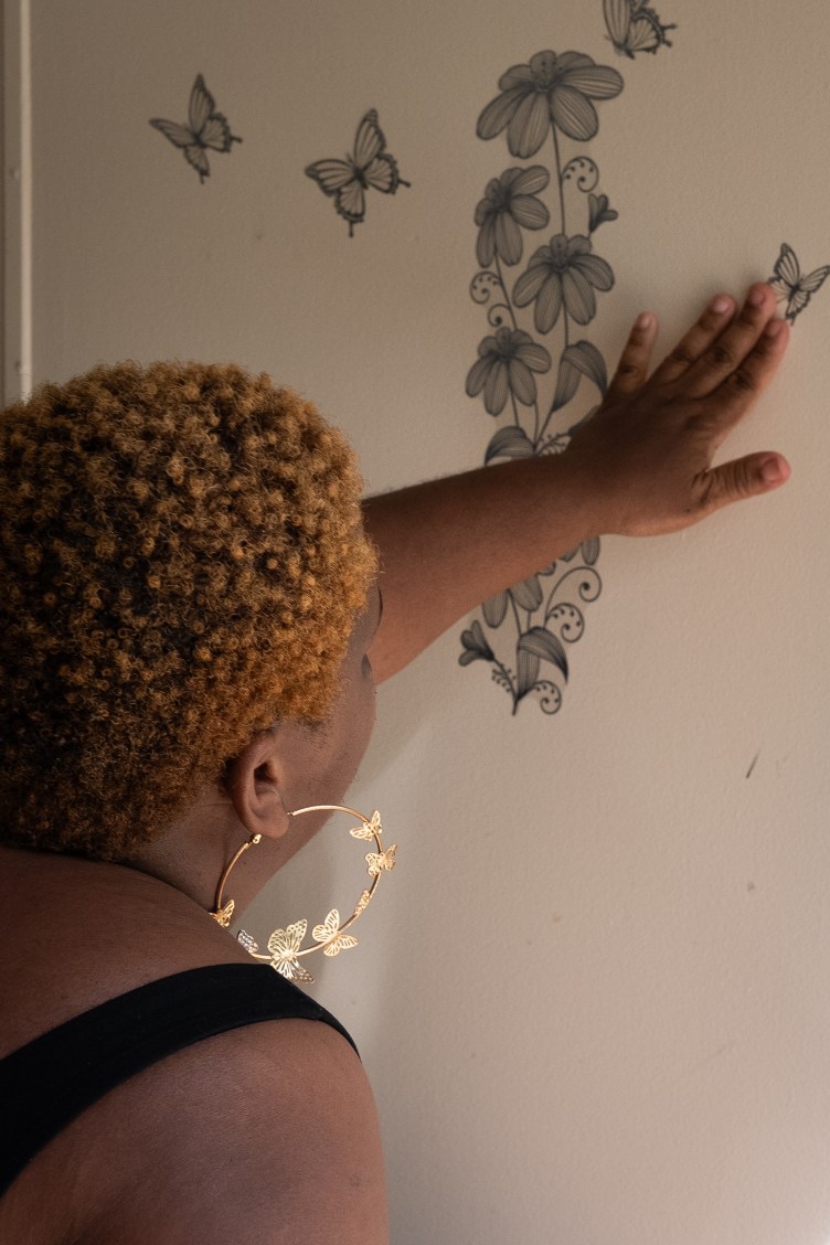 A woman with her back to the camera presses her hand on a butterfly decal pasted to the wall. There are other butterfly decals nearby surrounding a flower decal.
