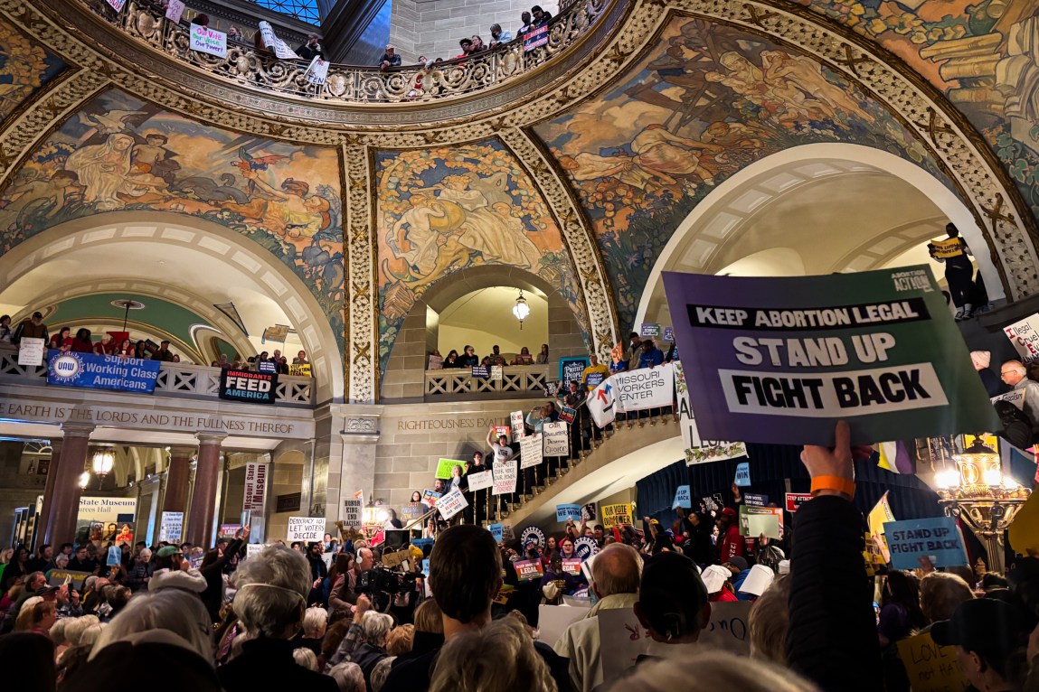Hundreds of people with protest signs fill a government building. A sign in the foreground reads, “Keep abortion legal. Stand up. Fight back.”