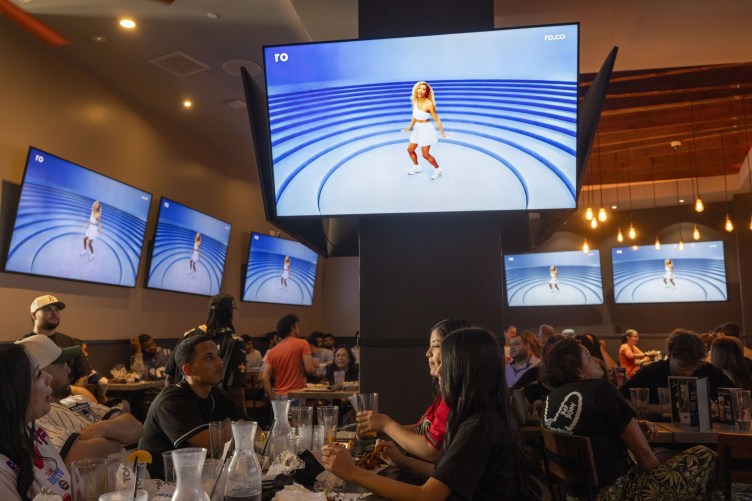 Six TVs showing a commercial with former tennis star Serena Williams above a packed restaurant with people dining and watching the screens.