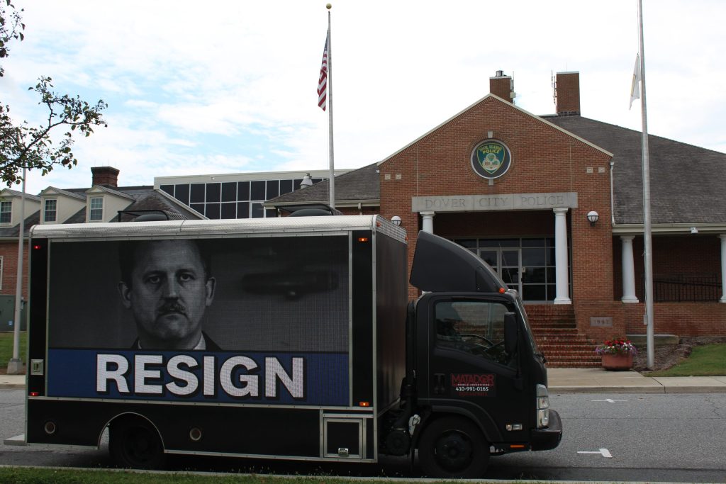 A black truck with the word RESIGN and a picture of Dover police chief out front of the Dover police department