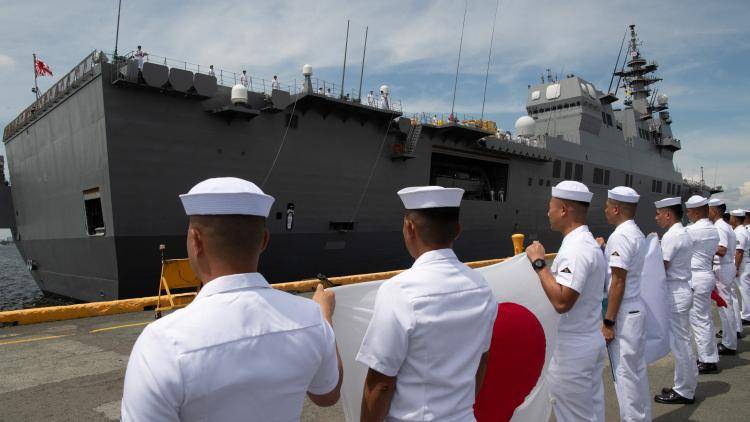 Philippine Navy sailors hold a Japanese flag in front of a Hyuga-class helicopter destroyer of the Japan Maritime Self-Defense Force, in Manila on 21 June 2025. (