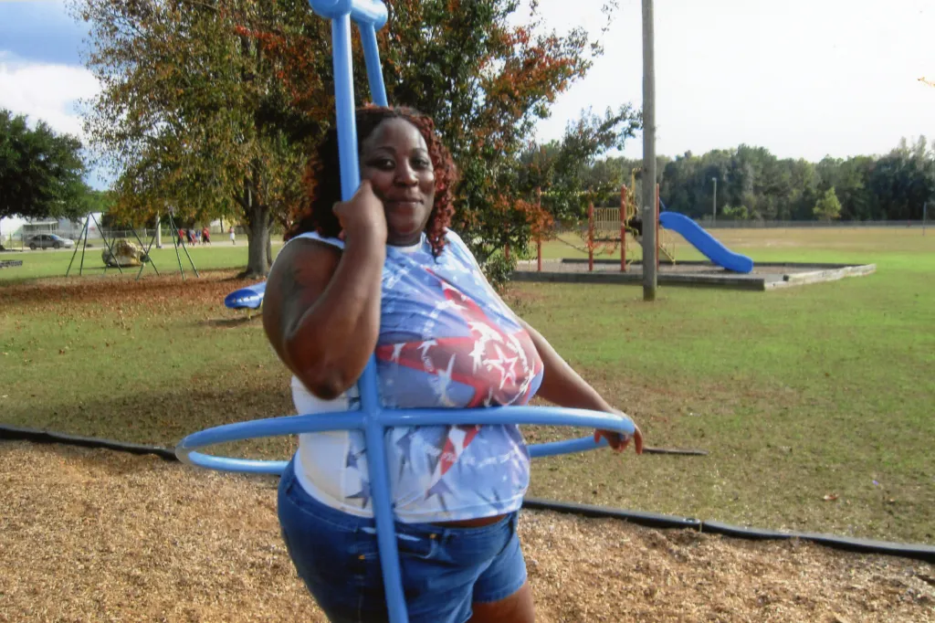 A woman poses in a blue jungle gym in a park. 