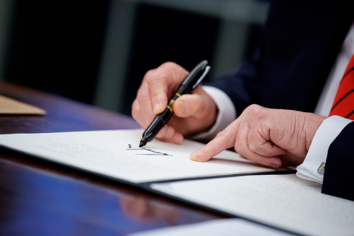 A close-up of the president’s hands, with a felt-tip pen in the right, atop a document.