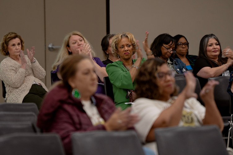 Women in rows of gray seats clap during a meeting.