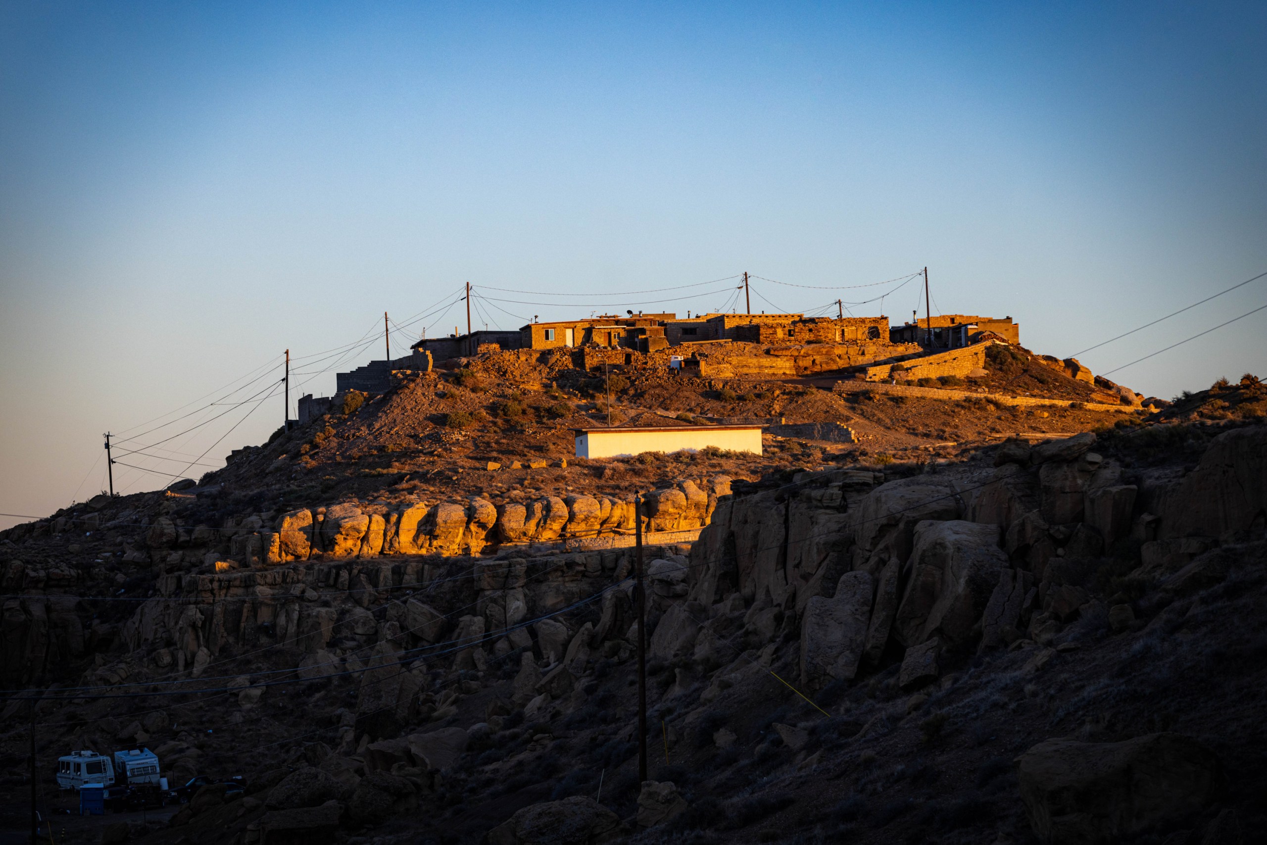A village of small, flat-roofed stone buildings sits atop a rocky, sunlit hill.