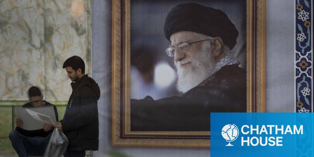 A man stands next to a portrait of Ayatollah Ali Khamenei