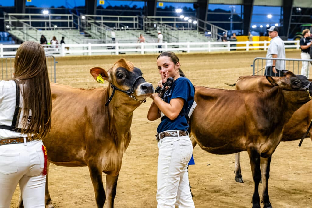 Cara Nacrelli puts up the peace sign while standing with her cow in the Open Dairy Cattle Show.