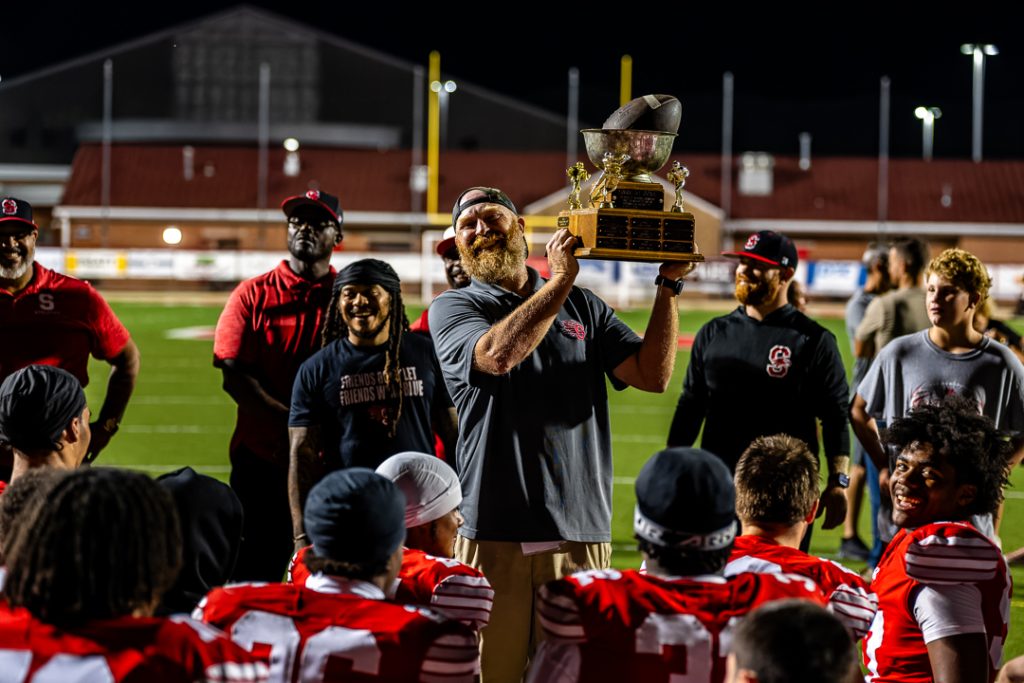 Eagles' head coach Mike Judy lifts the Harvest Bowl trophy during the teams' postgame huddle.