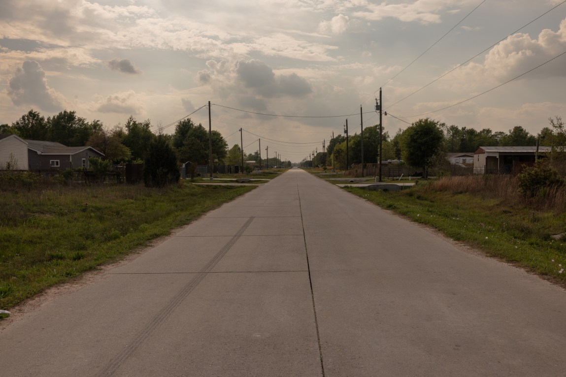 A road runs through a rural subdivision with houses and telephone poles and lines running alongside it. A lone black tire streak marks the road.