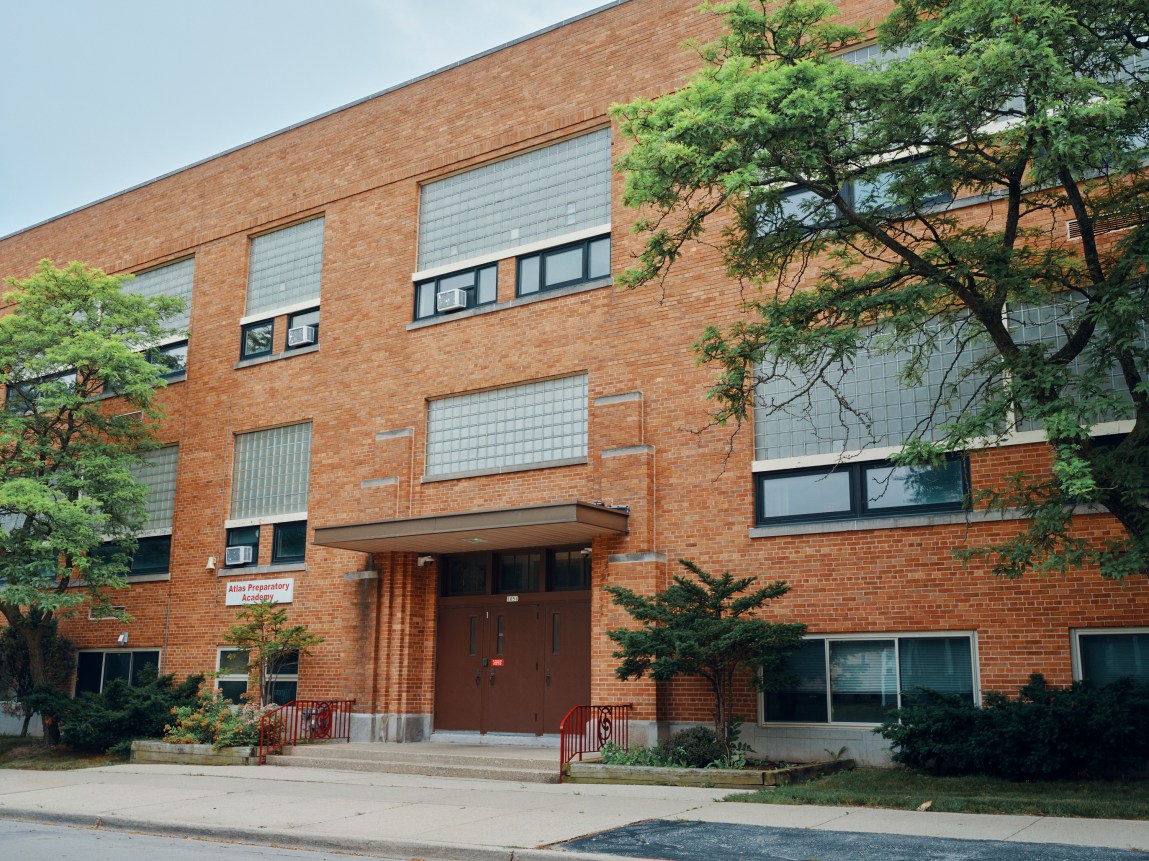A two-story brick building with a set of brown doors and a sign that says Atlas Preparatory Academy.