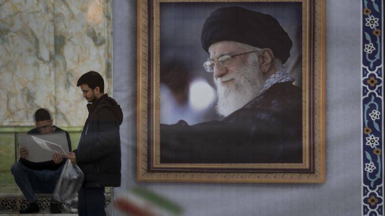 A man stands next to a portrait of Ayatollah Ali Khamenei