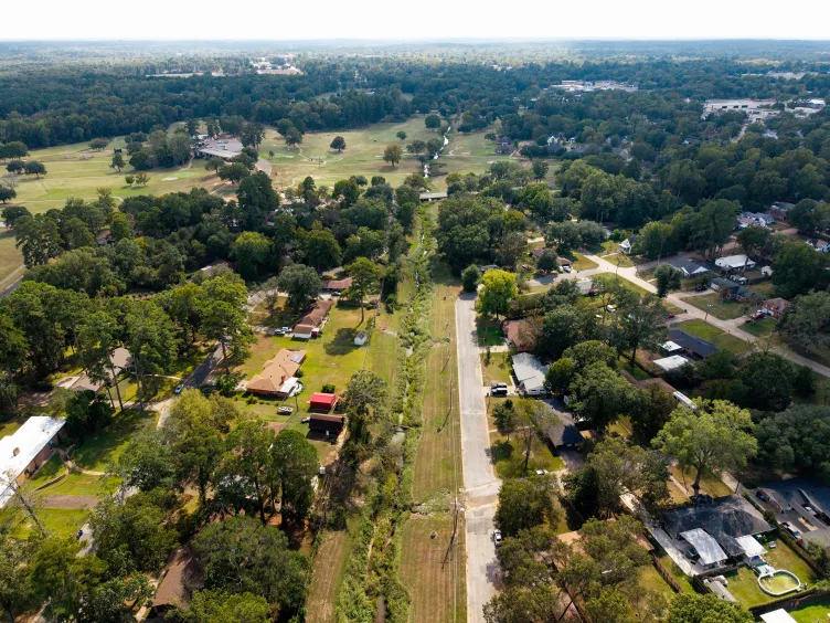 An aerial view of a rural town with a small stream running through trees and houses.