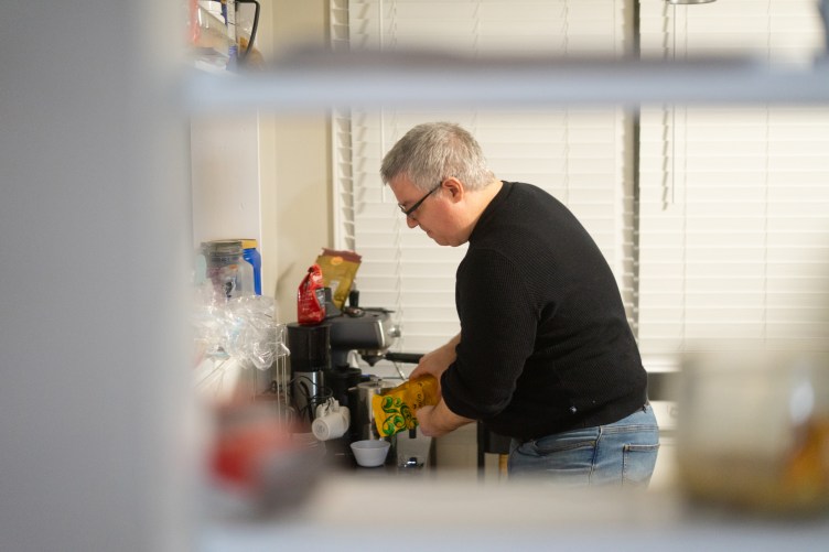 A white man with glasses makes coffee in his kitchen.