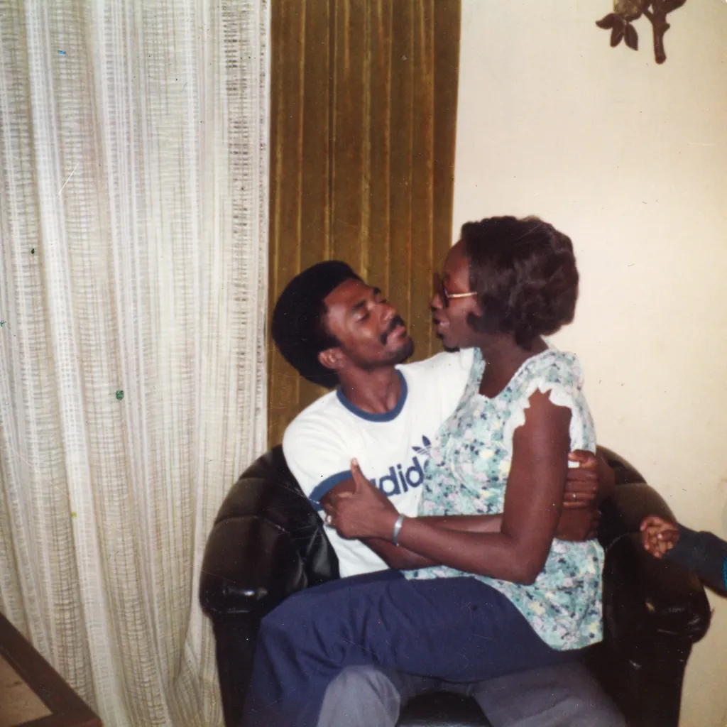 A man and a woman sit on a couch. The woman is sitting on the man’s lap and they are smiling at each other.
