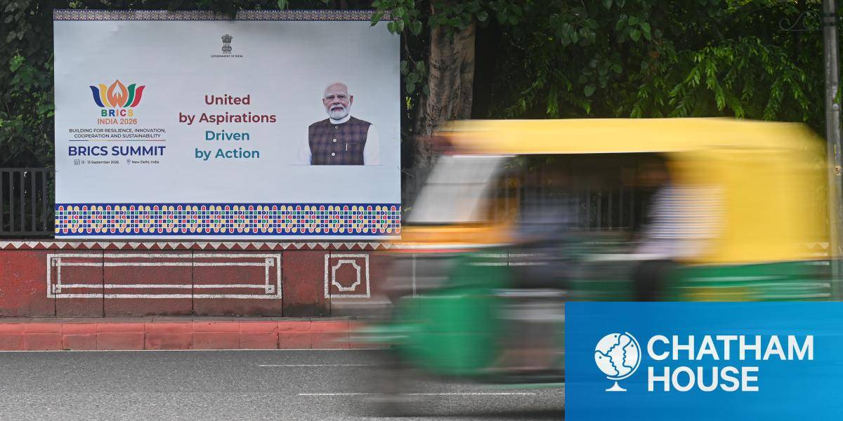 A yellow and green vehicle passes a poster of Prime Minister Modi promoting the 2026 BRICS conference