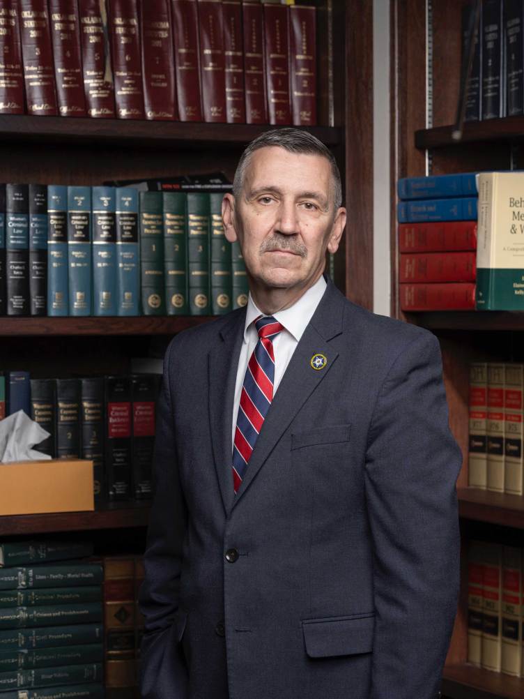 A man wearing a suit and a striped tie standing in a library of legal books.