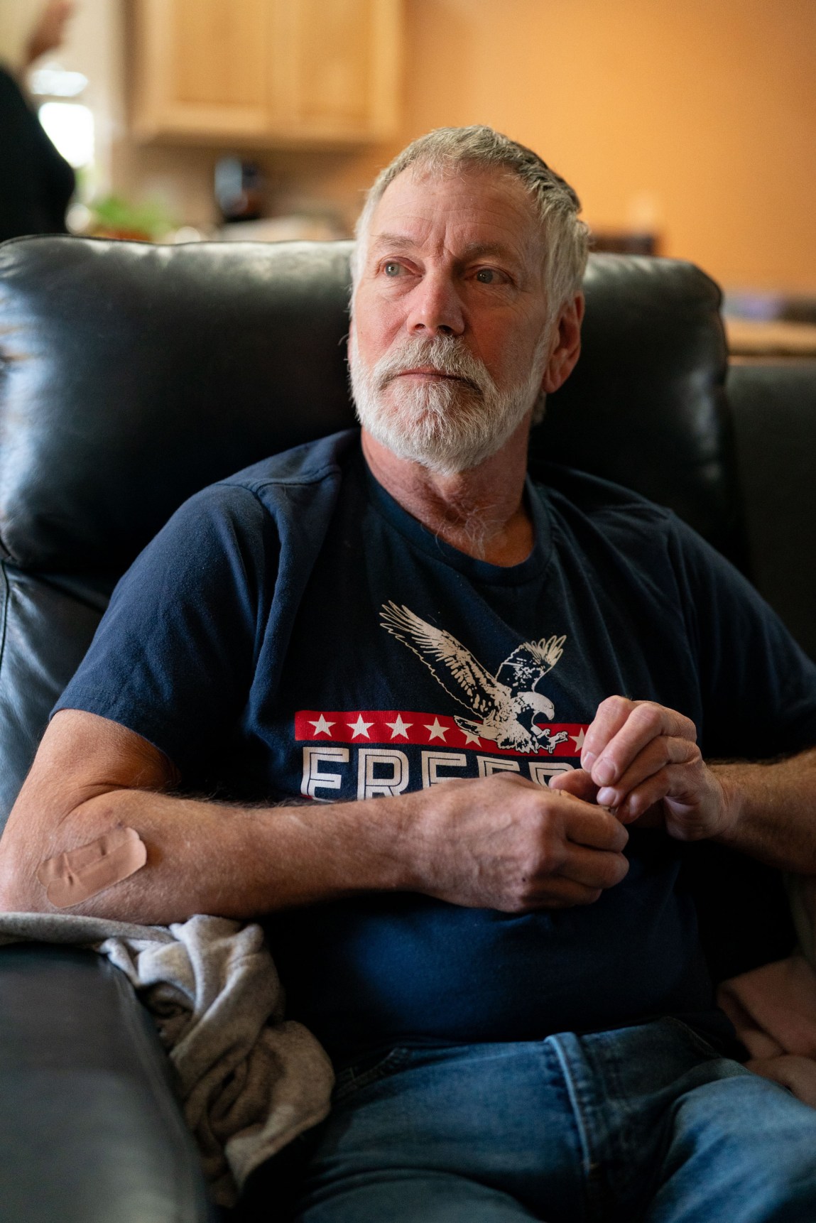 A white man sits in a leather chair with his hands in front of his chest. 