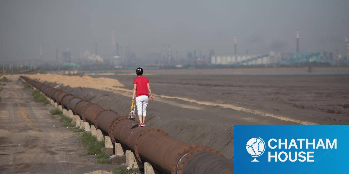 A woman standing on the banks of a 'toxic lake' surrounded by rare earth refineries 