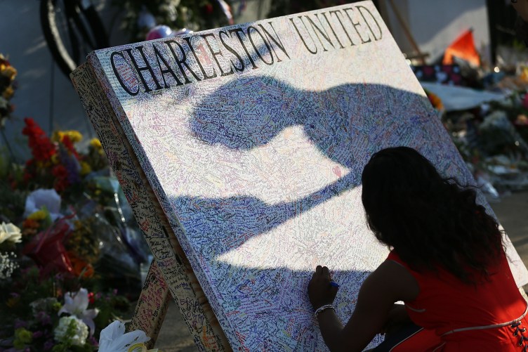 A woman kneels to write a message on a board with the words “Charleston United” that rests in front of flower bouquets.