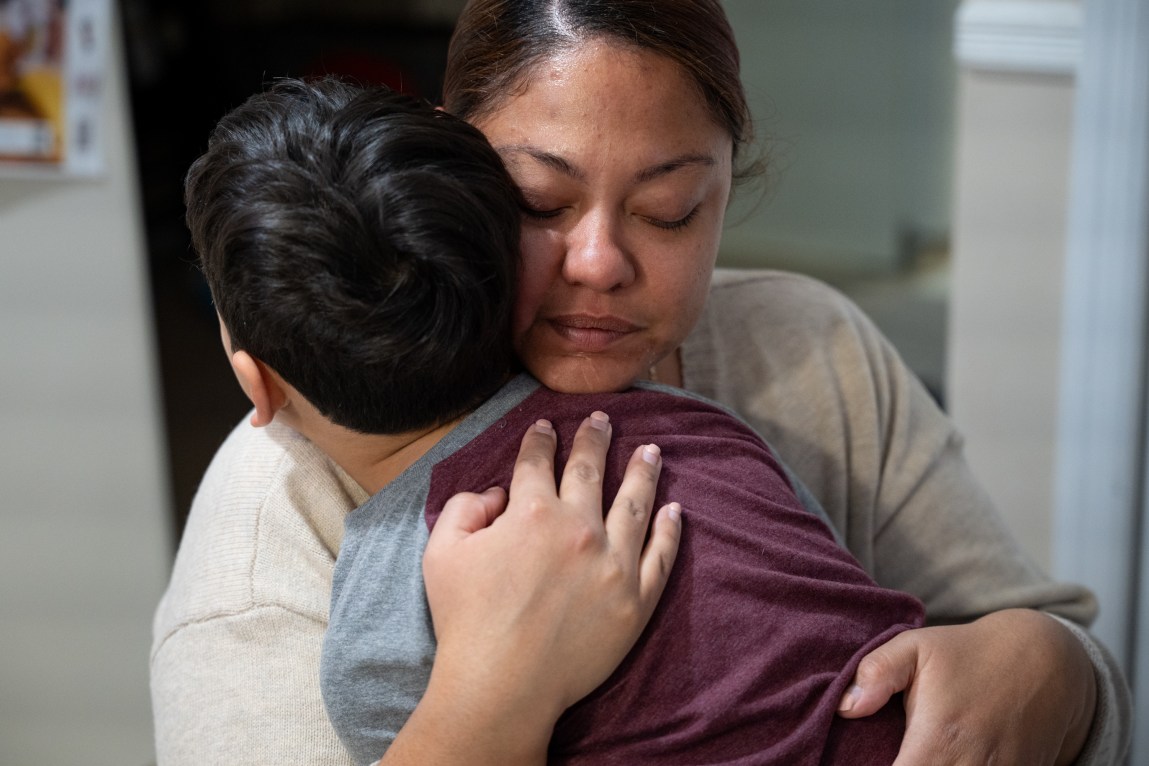 A woman wraps her arms around a young boy with her eyes closed.