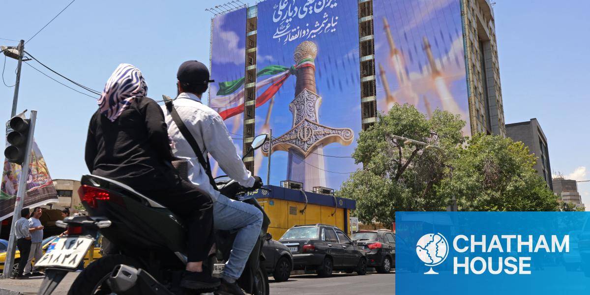a man and woman on a scooter approaching a billboard in Tehran