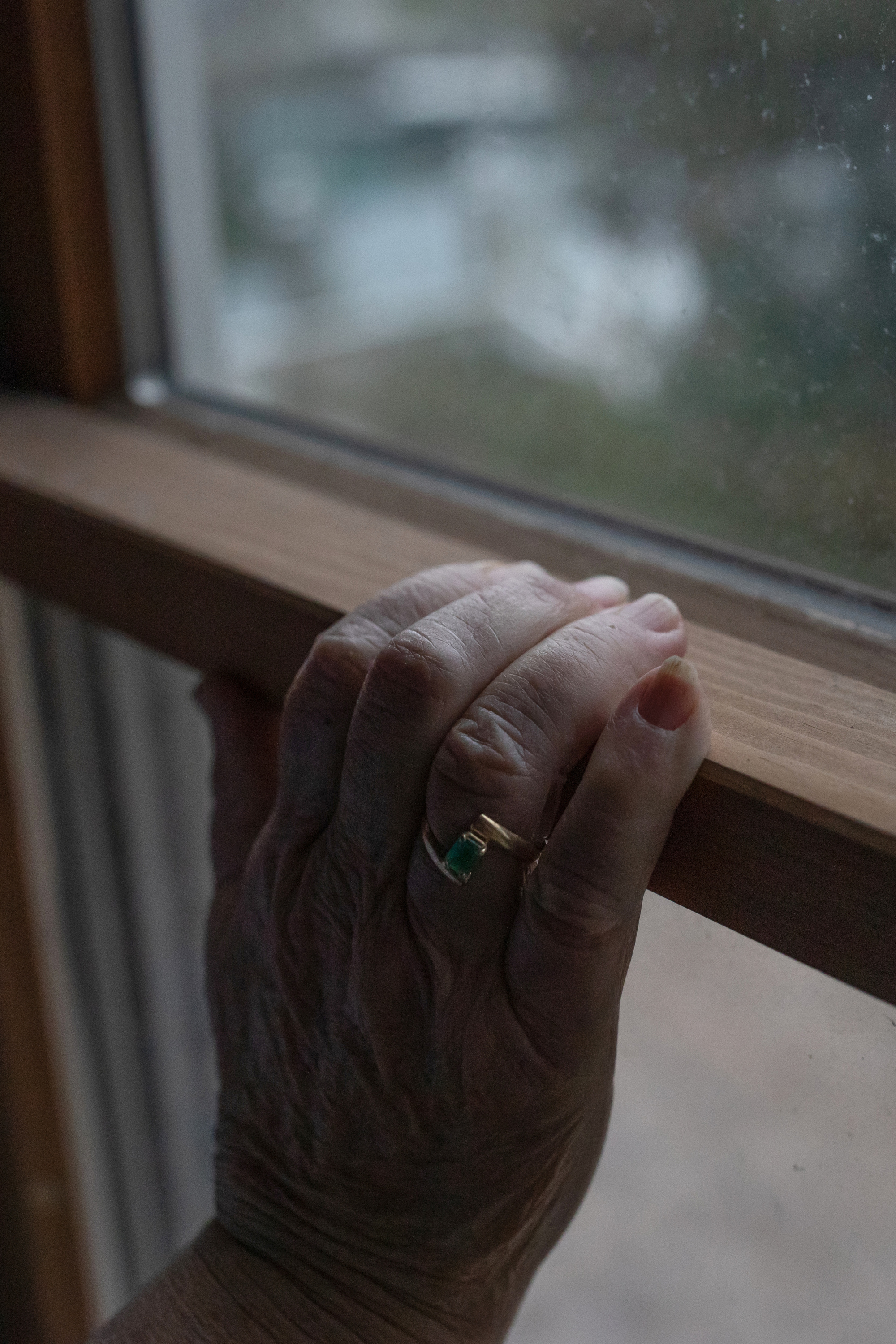 Durand’s right hand grips a wooden windowsill. She wears a ring on her ring finger.