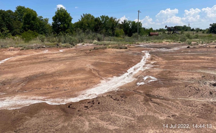 A depression like a river bed carves a path through a dirt landscape, with white salt residue covering the dirt in places.
