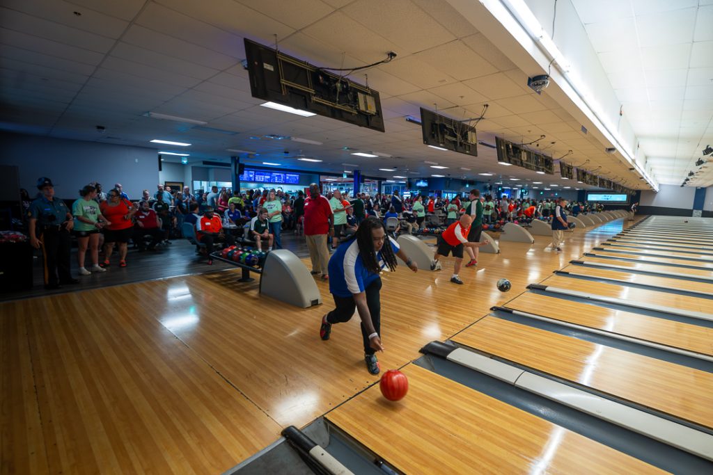 A couple of athletes take their turns bowling as a supporters fill the area behind the participants. 