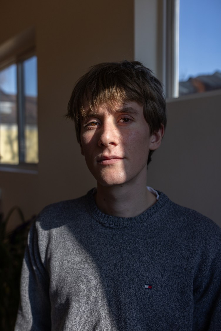 A head-and-shoulders portrait of a man in his 20s, looking at the camera with a neutral expression, lit dramatically.