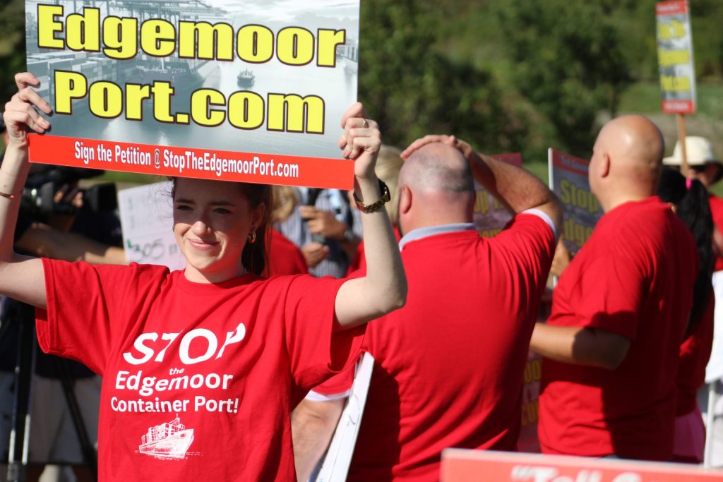 Protestors dressed in red outside of the Edgemoor port expansion project in Wilmington hold signs that say EdgemorePort.com and shirts that say "Stop the Edgemoor Port."