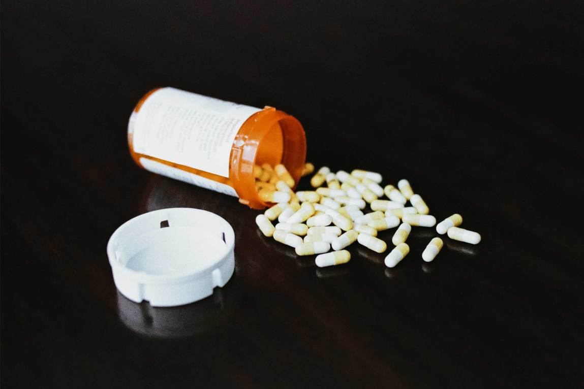 An orange prescription bottle open and overturned, spilling pills onto a black surface.