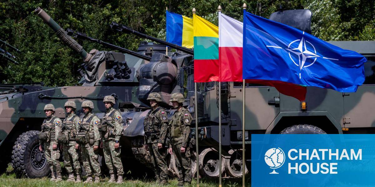Polish and Romanian soldiers stand next to military vehicles and a Polish and NATO flag.