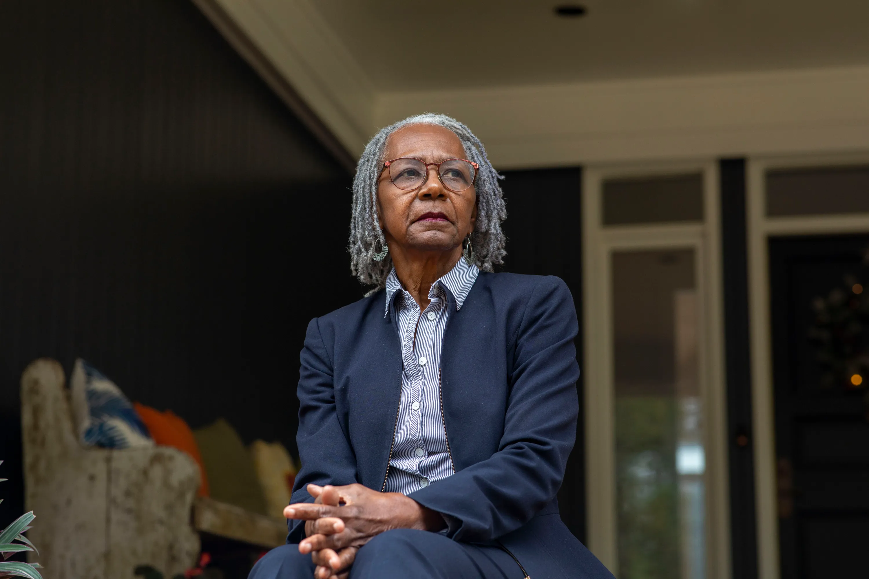 A woman with gray hair, wearing glasses and a suit, looks off into the distance.