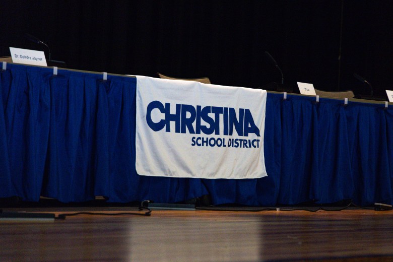 A Christina School District banner sits at the table reserved for school board members during a public meeting in July 2025.