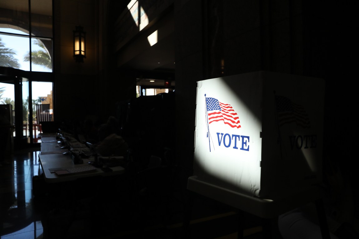 A voting booth with an American flag image lit in a dark room.