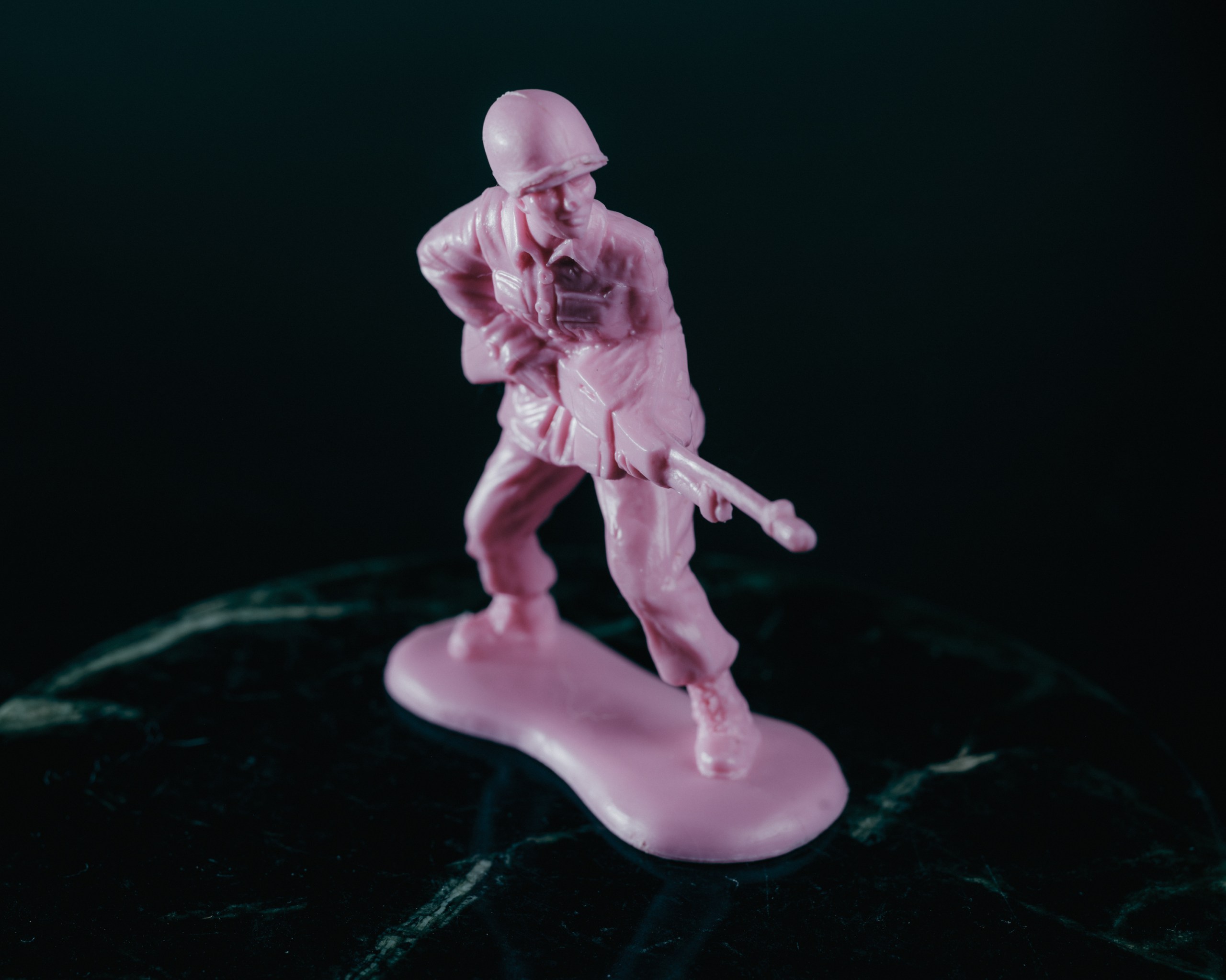 A pink plastic figurine of a soldier pointing a firearm rests on a green marble table.