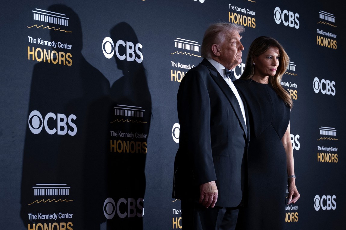 A man and a woman wearing formal attire pose in front of a backdrop that is decorated with logos for the Kennedy Center and CBS.