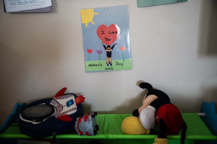 A handmade sign for Mother’s Day above a child’s cot with toys and a stuffed Mickey Mouse doll.